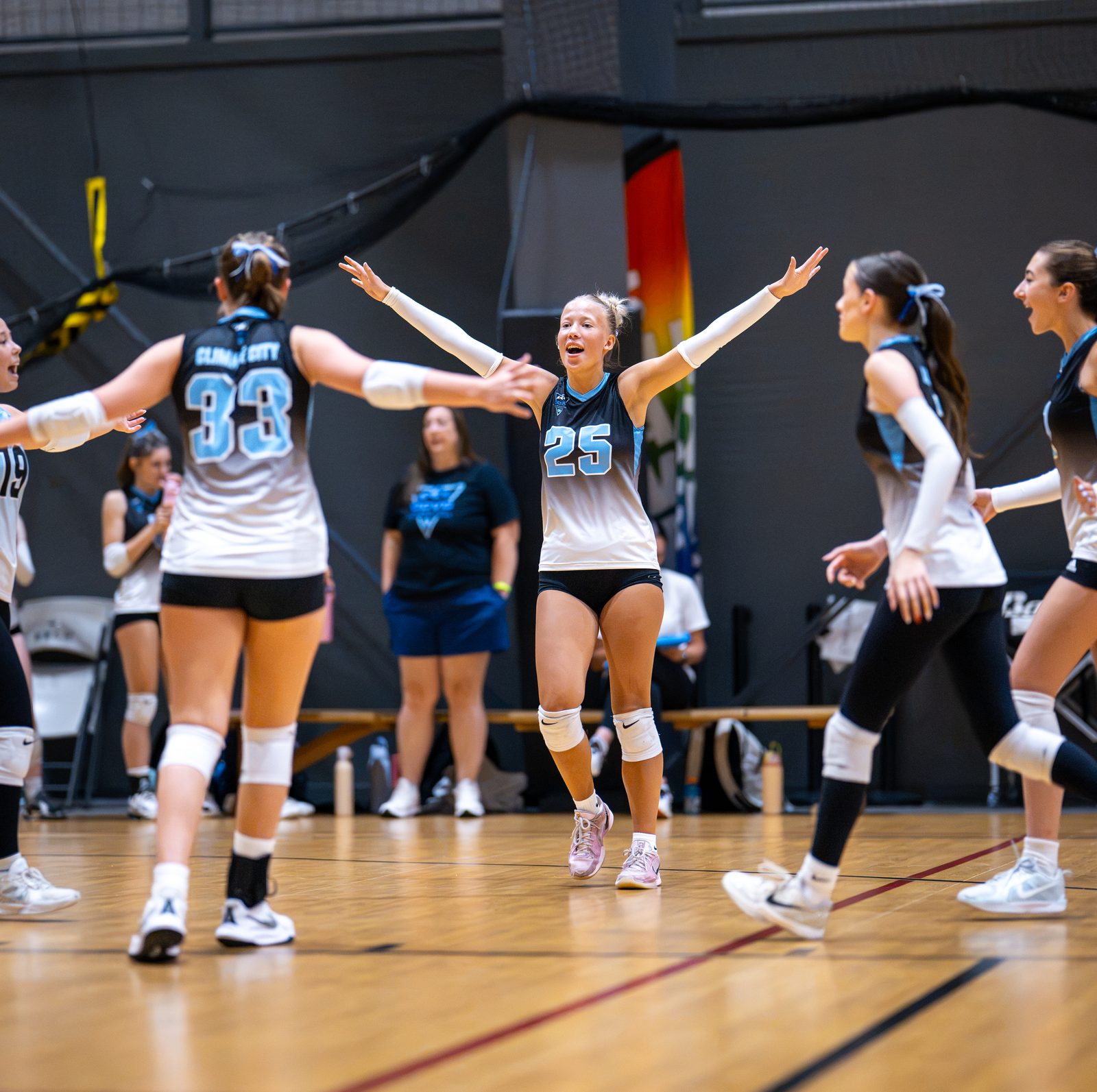 Players in light blue and black celebrate with arms out after a point