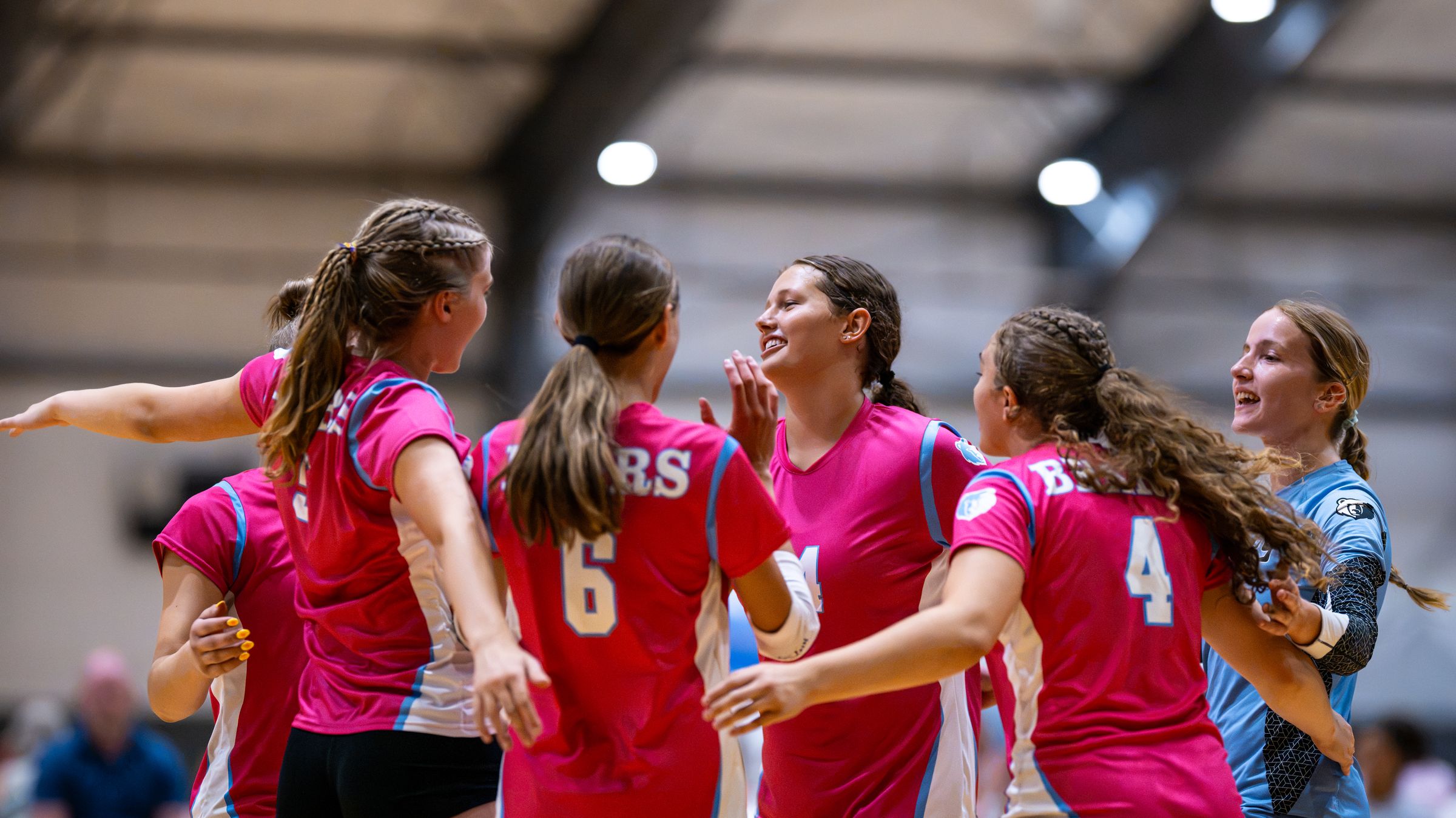 A team in pink jerseys cheers together after a point